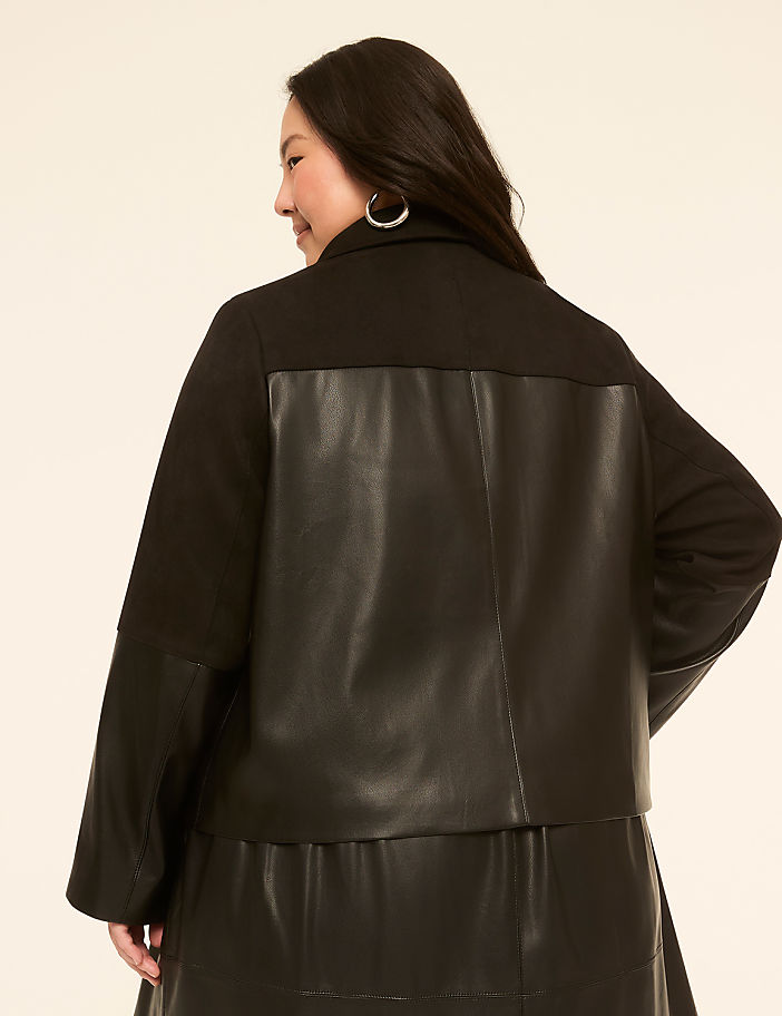 A woman in a black jacket with leather accents stands against a plain, light-colored background.