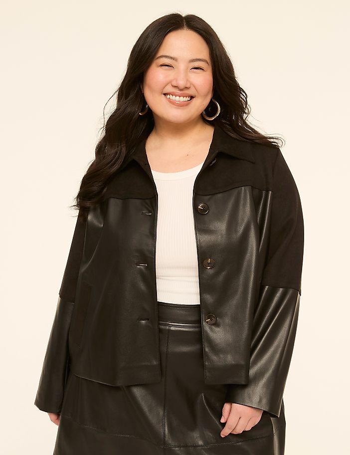 A smiling woman with dark hair wears a black jacket over a white top and black skirt against a plain, light-colored background.