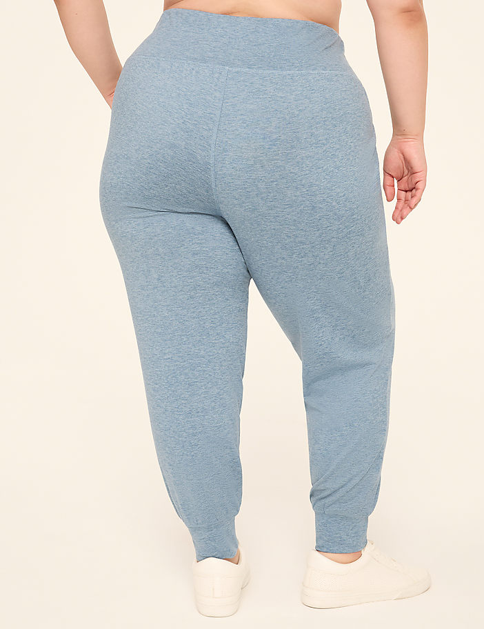 A person wearing light blue sweatpants and white sneakers stands against a plain, light-colored background.