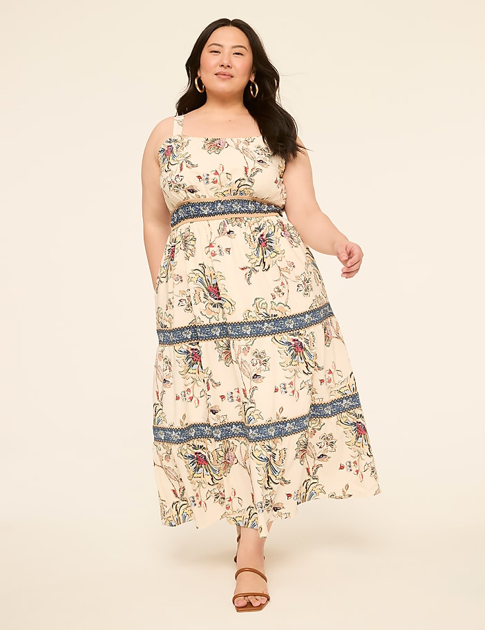 A woman in a floral print dress stands against a plain, light-colored background.