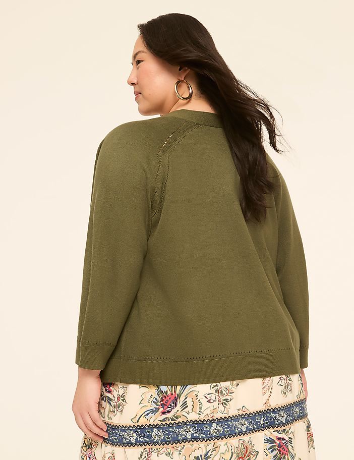 A woman in a green cardigan and patterned skirt stands against a plain, light-colored background.