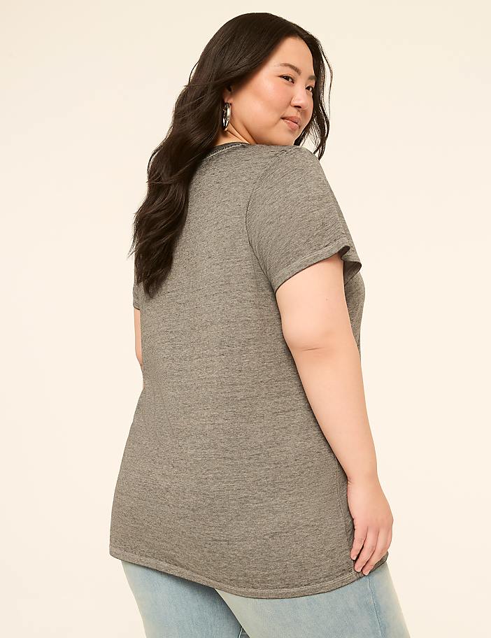 A woman in a grey t-shirt and jeans poses against a plain, light-colored background.