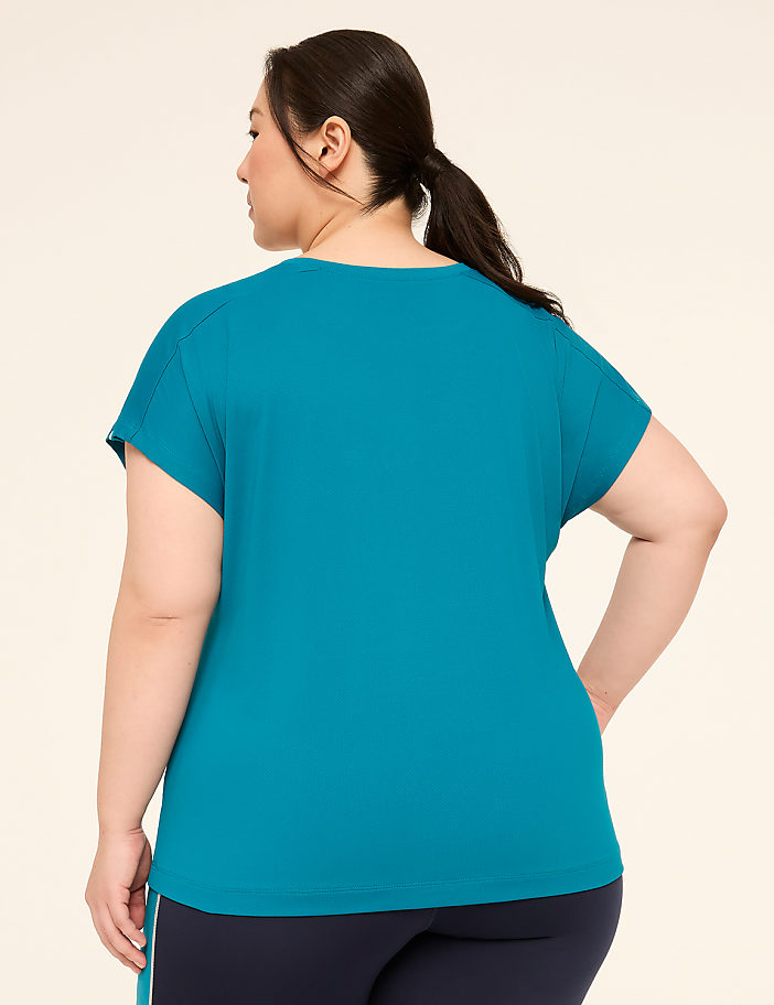 A woman in a teal t-shirt and navy leggings stands against a plain beige background.