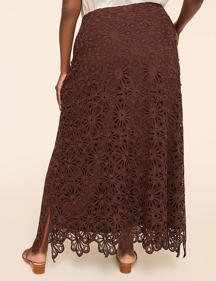 A person in a brown lace maxi skirt with a slit stands against a plain, light-colored background.