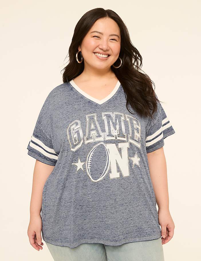 A smiling woman in a blue "GAME ON" t-shirt stands against a plain, light-colored background.