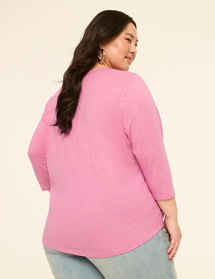 A woman in a pink shirt and jeans stands against a plain, light-colored background.