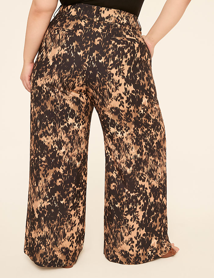 A person wearing wide-leg pants with a brown and black abstract pattern stands against a plain, light-colored background.