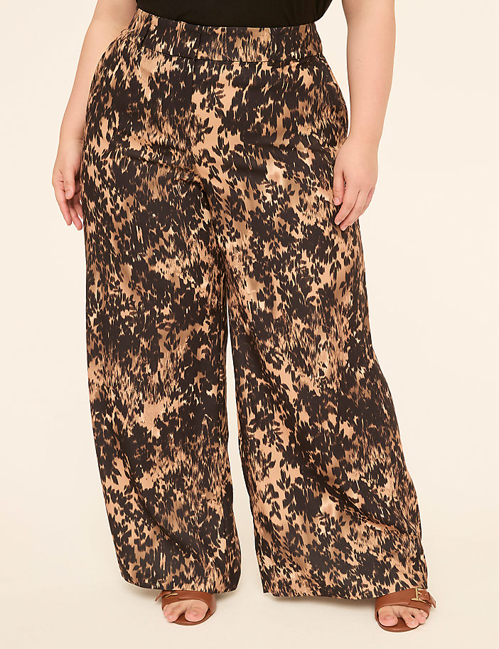 A person stands in wide-leg, abstract-print pants and sandals against a plain, light-colored background.