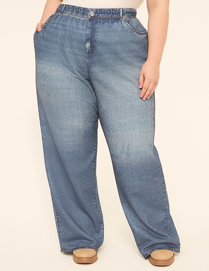 A person wearing loose-fitting denim jeans stands against a plain, light-colored background.