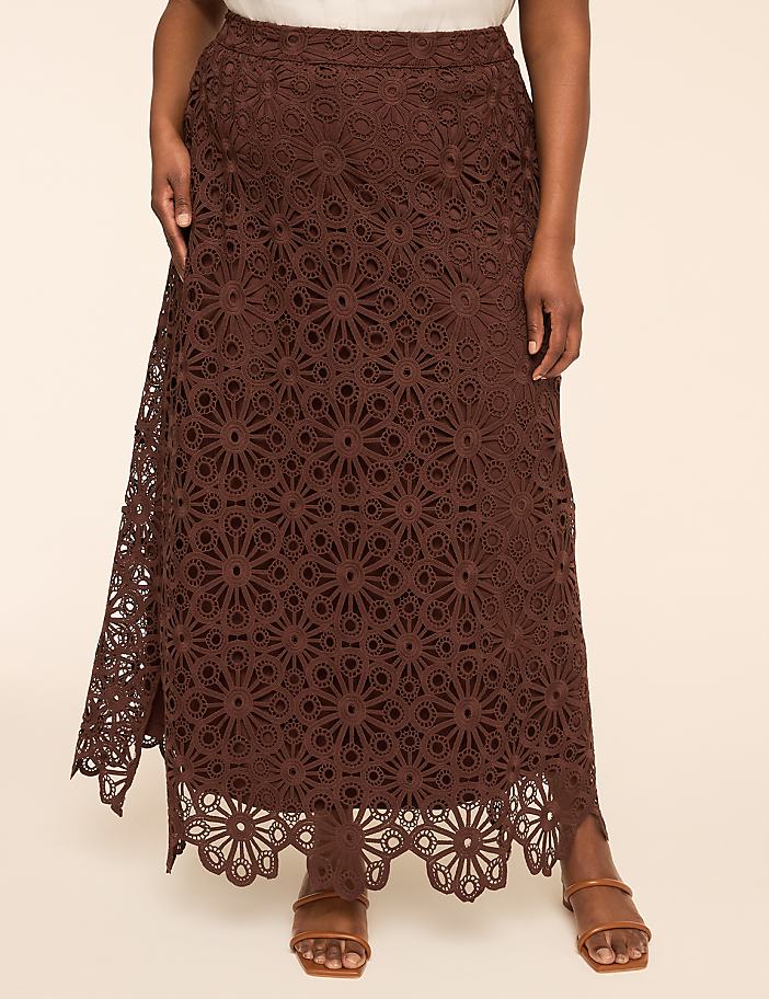A woman in a brown lace maxi skirt stands against a plain beige background.