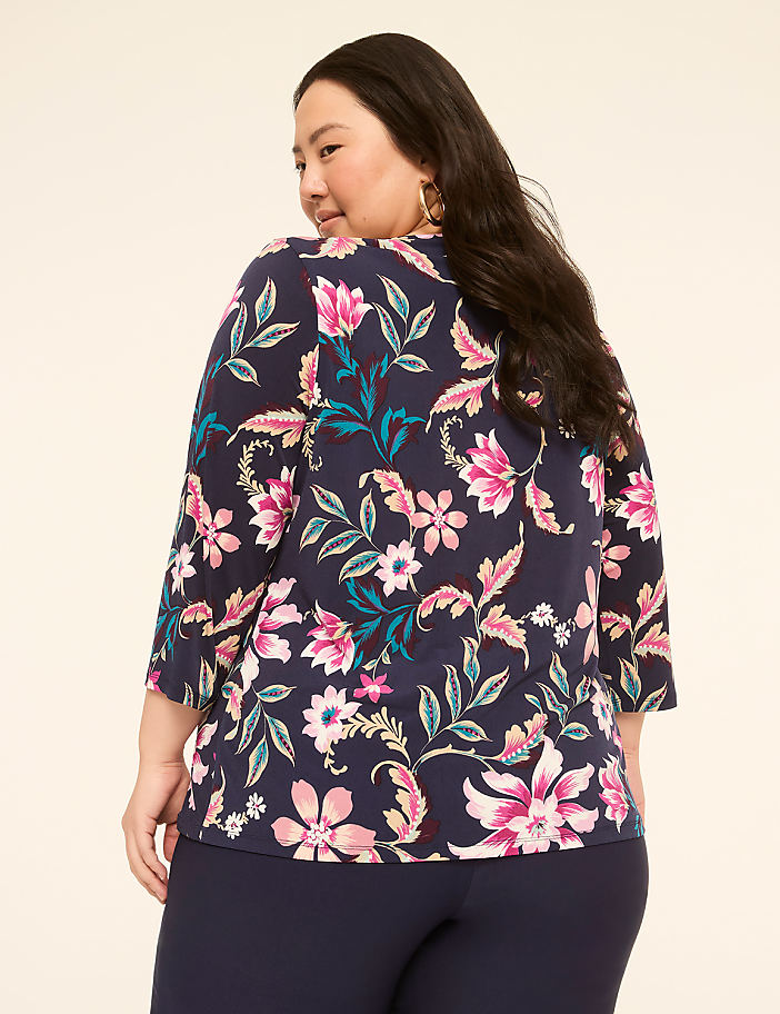 A woman with dark hair, wearing a navy blue floral-patterned top and navy blue pants, is shown from the back against a plain, light-colored background.