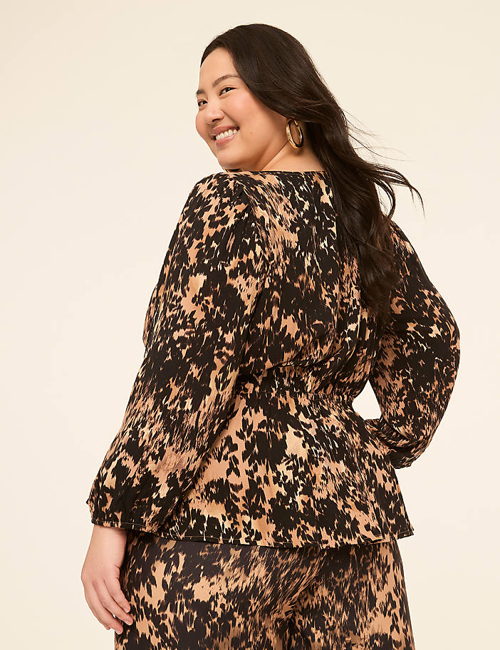 A woman with dark hair and a patterned top smiles over her shoulder against a plain, light-colored background.