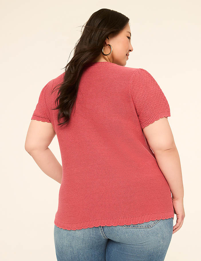 A woman in a pink top and jeans stands against a plain, light-colored background.