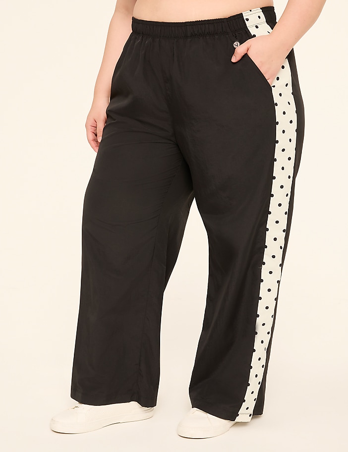 A person wearing black wide-leg pants with a white side stripe featuring black polka dots stands against a plain, light-colored background.