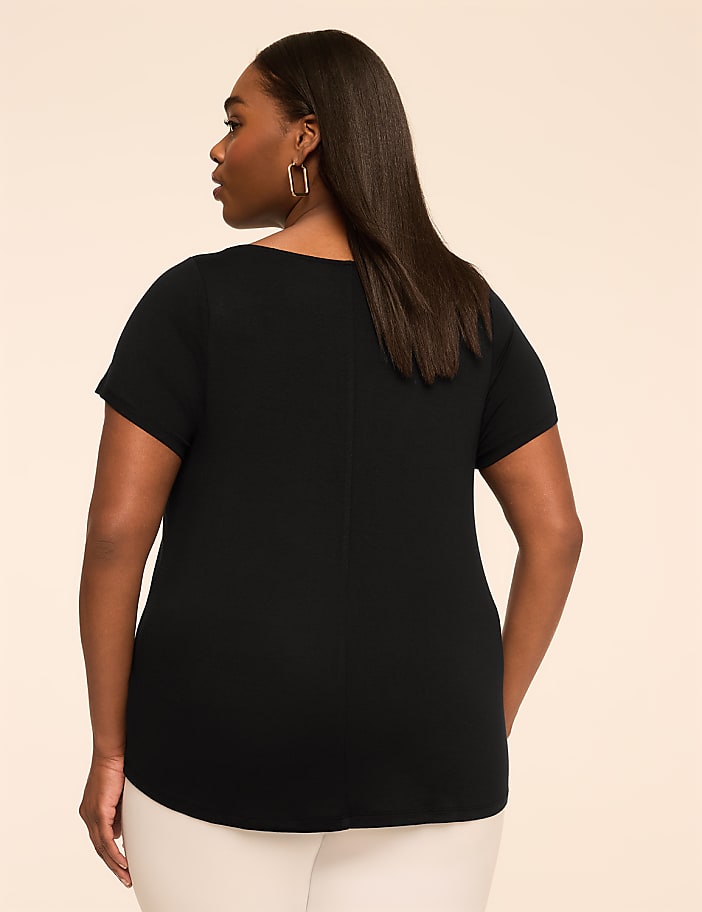 A woman in a dark brown shirt and light pants stands against a plain, peachy background.
