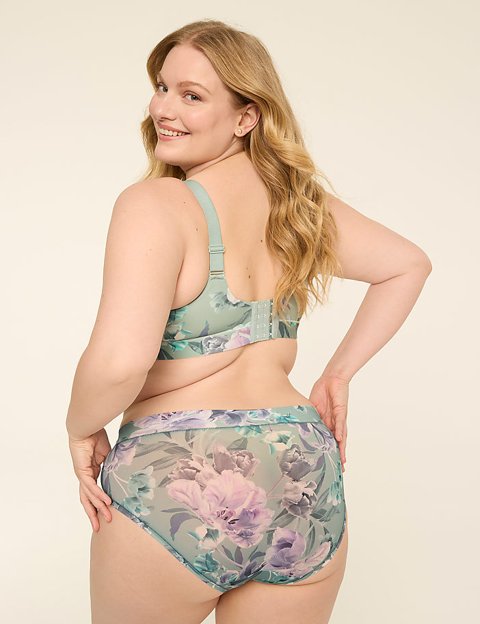 A woman in floral lingerie smiles over her shoulder against a plain, light background.