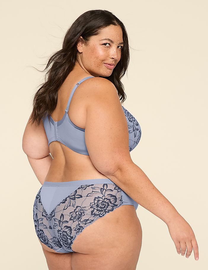 A woman in a blue lace bra and matching underwear poses against a plain, light background.