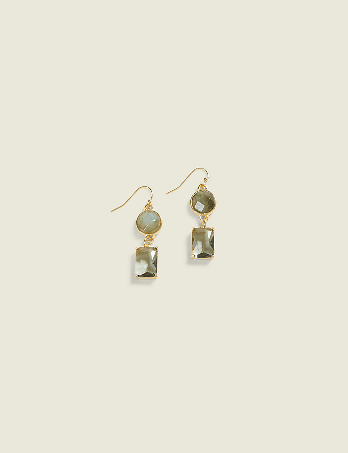 A pair of gold earrings with green oval and rectangular stones hang against a plain, light beige background.