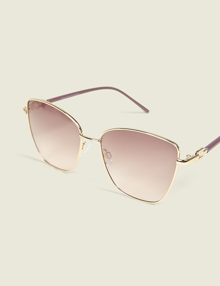 A pair of rose-gold cat-eye sunglasses with gradient lenses rests on a pale yellow background.