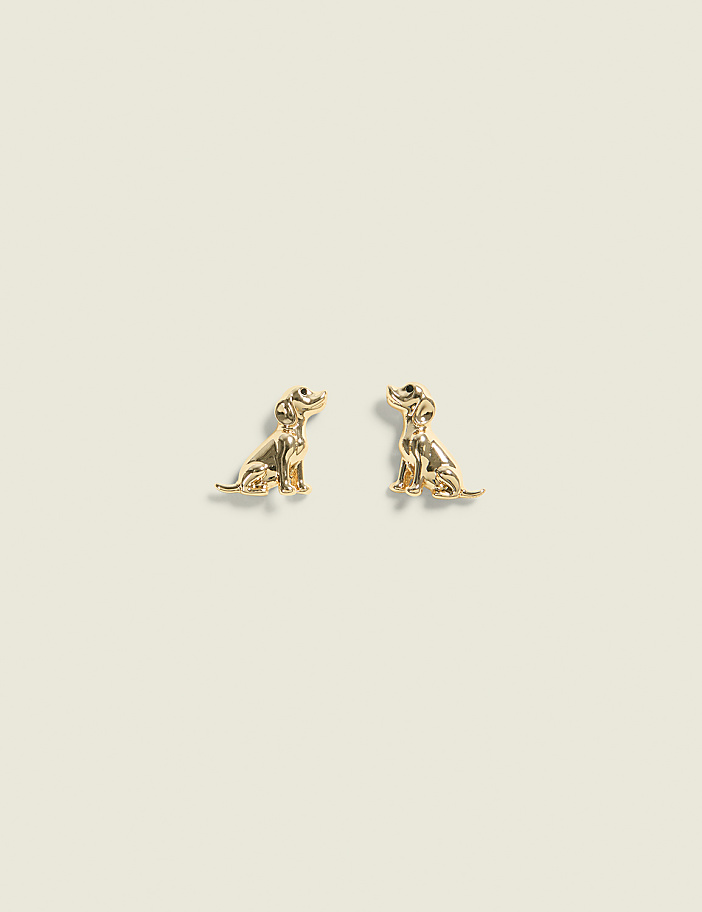 Two golden dog-shaped earrings sit on a plain, light-colored background.