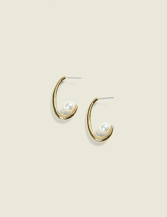 A pair of gold hoop earrings, each with a single pearl, are displayed against a soft, muted background.