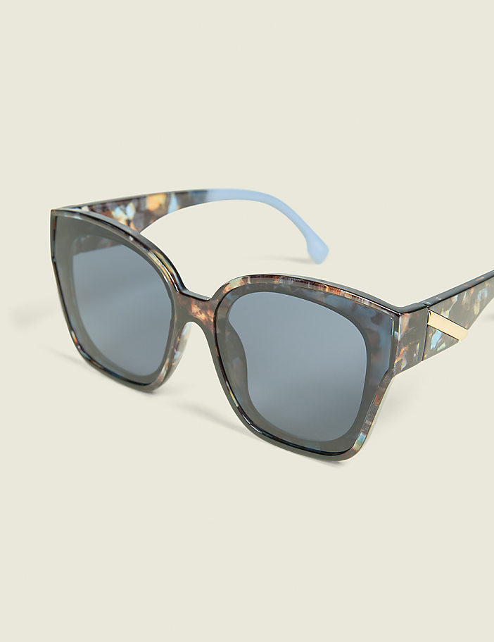 A pair of stylish, patterned sunglasses with blue temples rests on a plain, light-colored background.