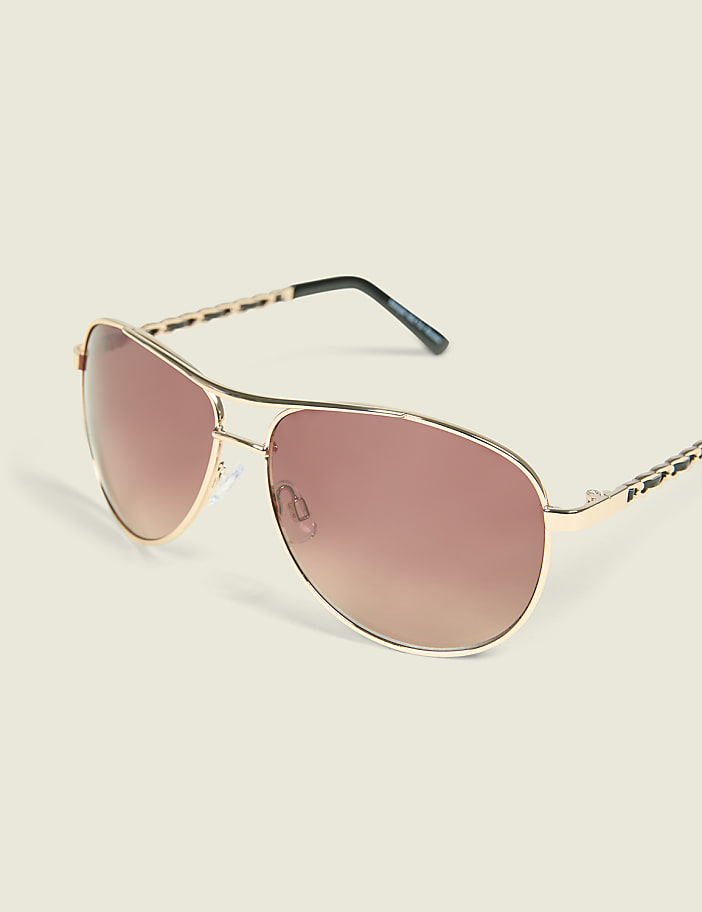 Gold aviator sunglasses with gradient brown lenses rest on a plain, light-colored surface.