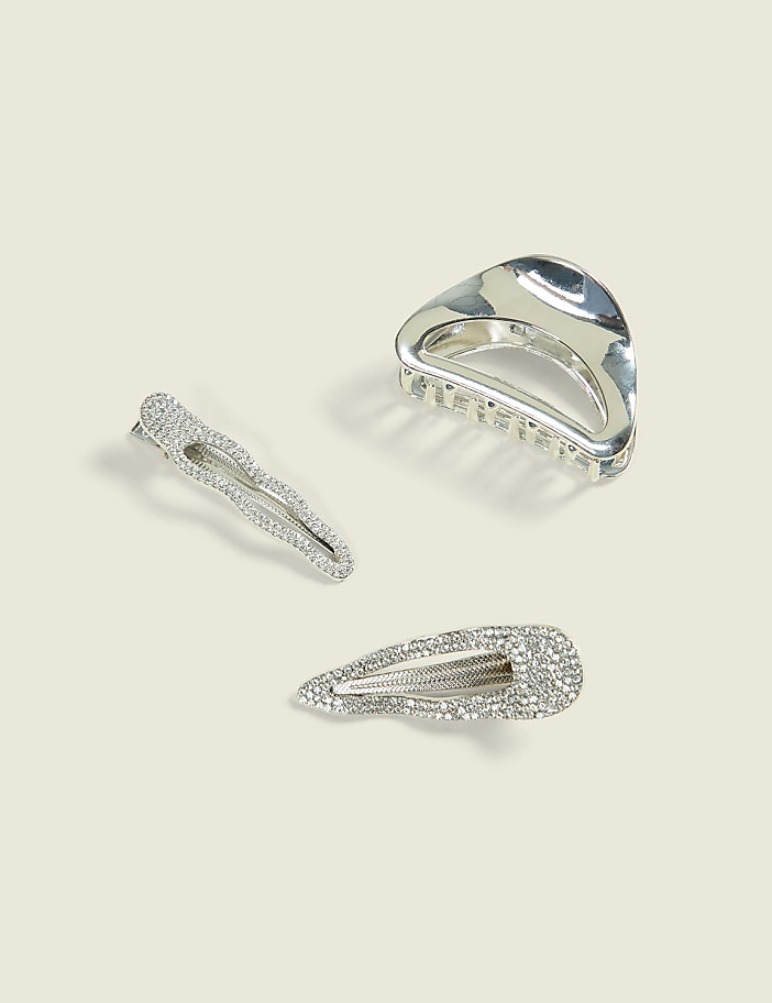 Three sparkly silver hair clips, two barrettes and one claw clip, rest on a plain cream background.