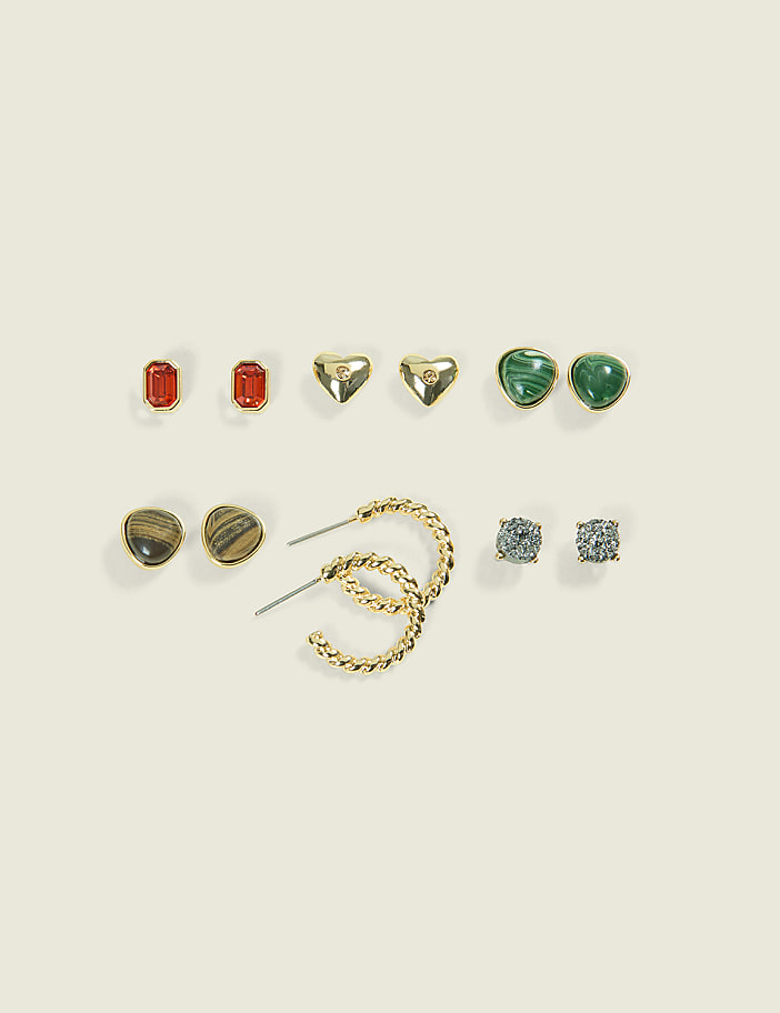 A collection of assorted earrings, including studs and hoops, are arranged on a plain, light-colored background.