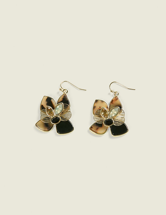 A pair of floral-shaped earrings with tortoiseshell and black petals and a light green gem dangle against a plain, light beige background.
