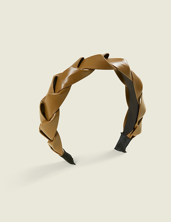 A braided tan headband with a black interior sits on a plain, light beige background.