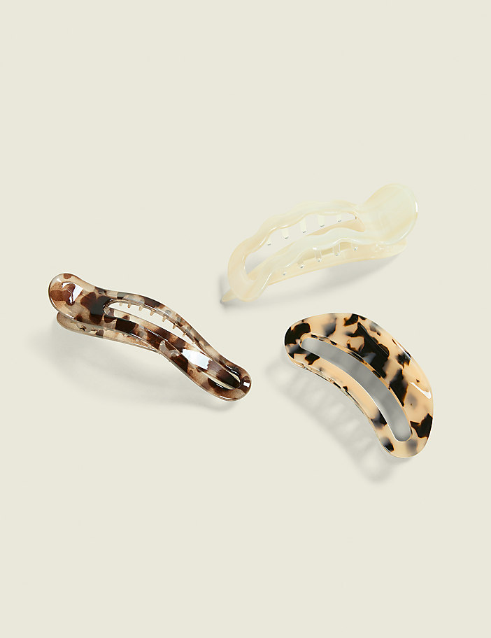 Three claw hair clips with tortoiseshell, leopard print, and translucent finishes rest on a pale, neutral background.