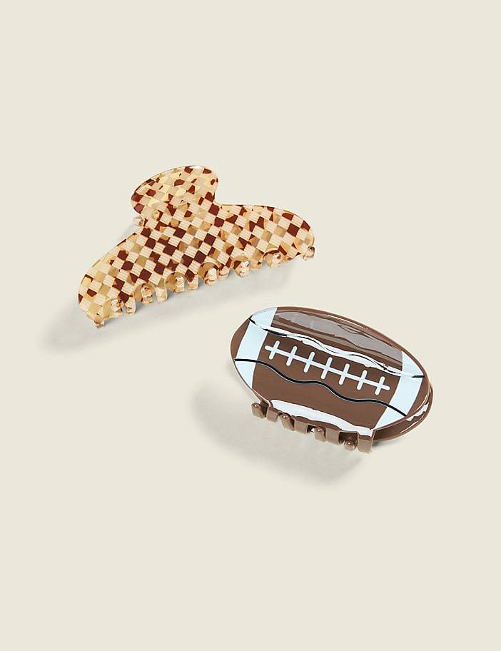 Two hair clips, one a checkered pattern and the other shaped like a football, rest on a light beige background.