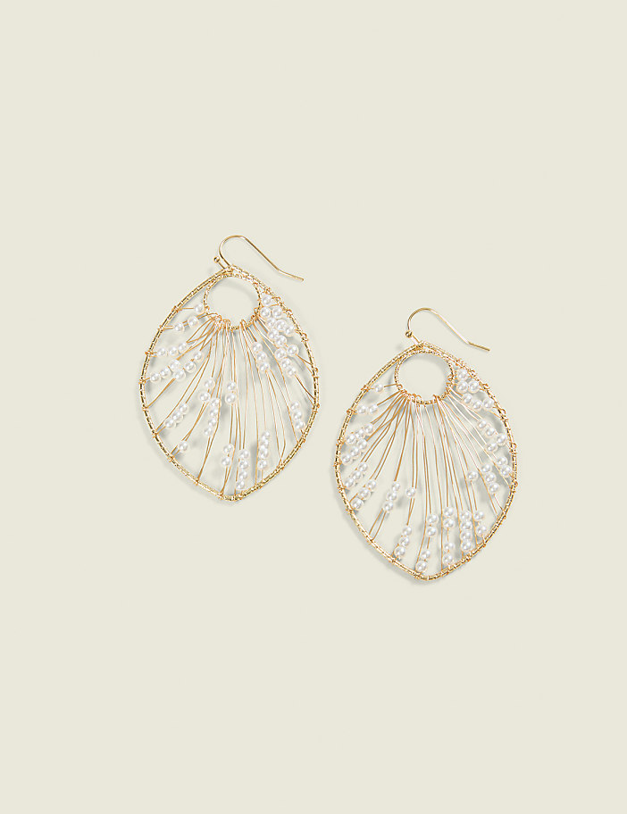 A pair of delicate, gold-toned leaf-shaped earrings with white beaded accents hang against a soft, pale yellow background.