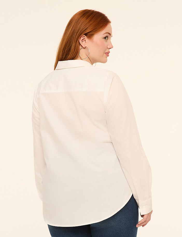 A woman with red hair, wearing a white collared shirt and blue jeans, stands against a plain, light-colored background.