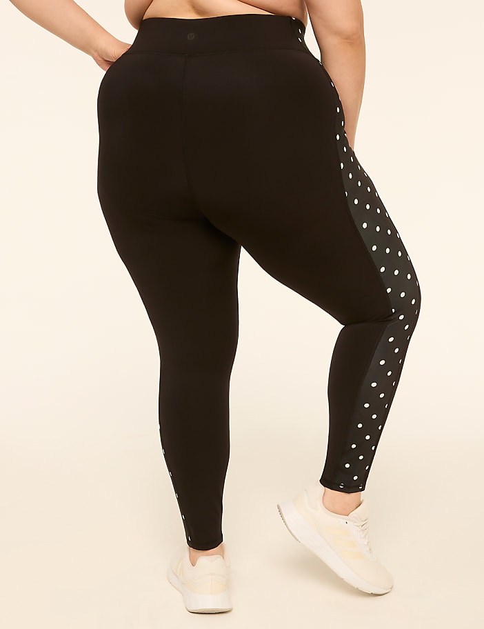 A person wearing black leggings with a polka dot pattern on the side stands against a plain, light-colored background.