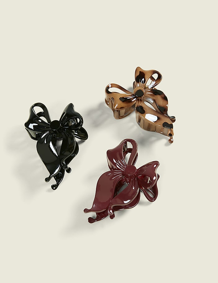 Three decorative bow-shaped hair clips, one black, one leopard print, and one burgundy, are arranged on a plain, light-colored background.