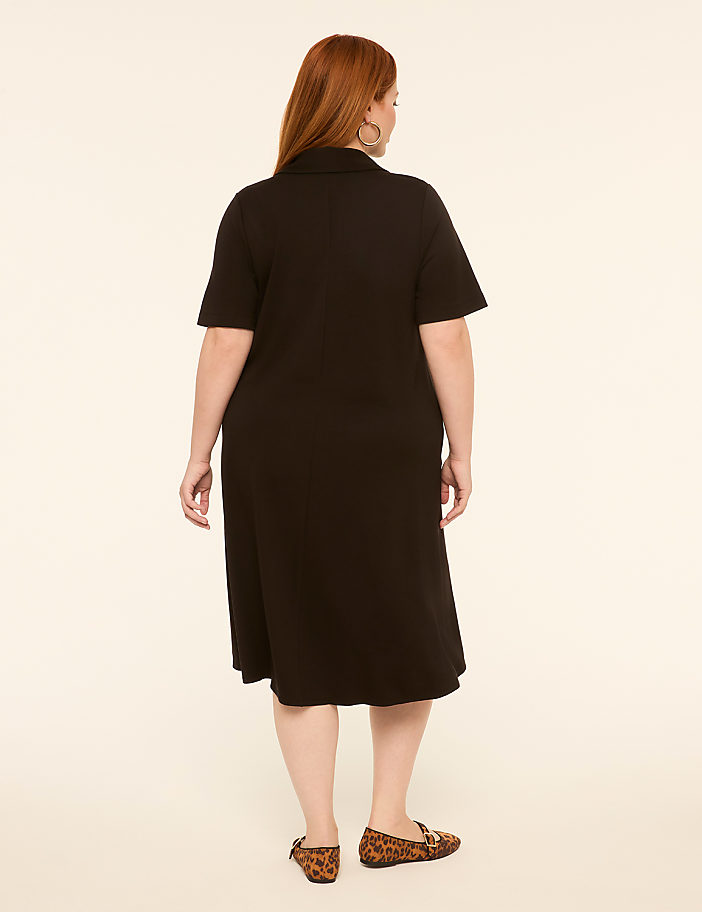 A woman in a black dress stands against a plain, light-colored background.