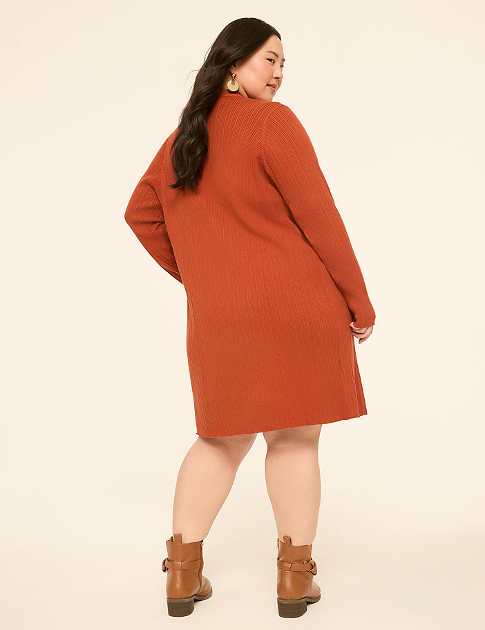 A woman in a rust-colored ribbed dress and brown ankle boots stands against a plain, light-colored background.