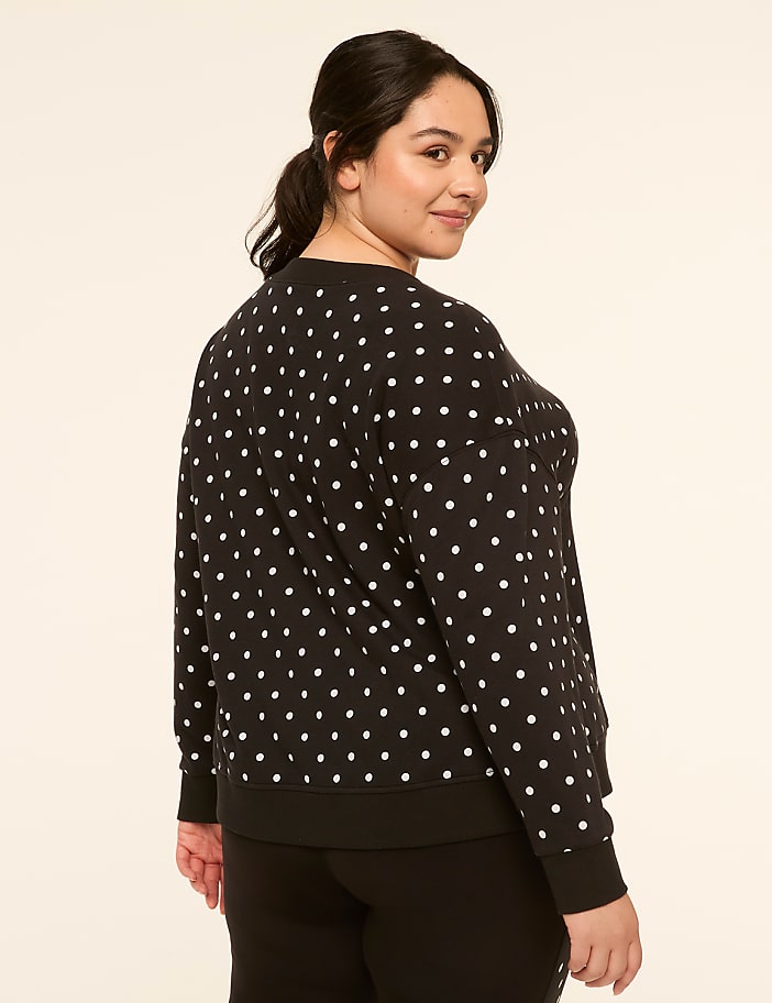 A woman in a black and white polka dot sweatshirt stands against a plain, light-colored background.
