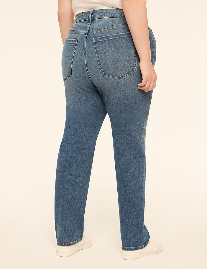 A person wearing blue jeans and white sneakers stands against a plain, light-colored background.