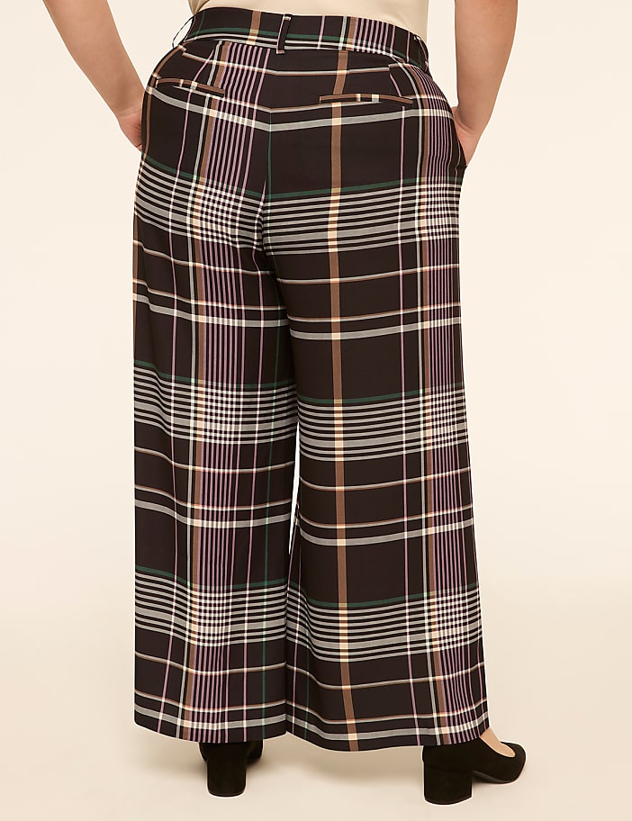 A person wearing wide-leg plaid pants stands against a plain, light-colored background.