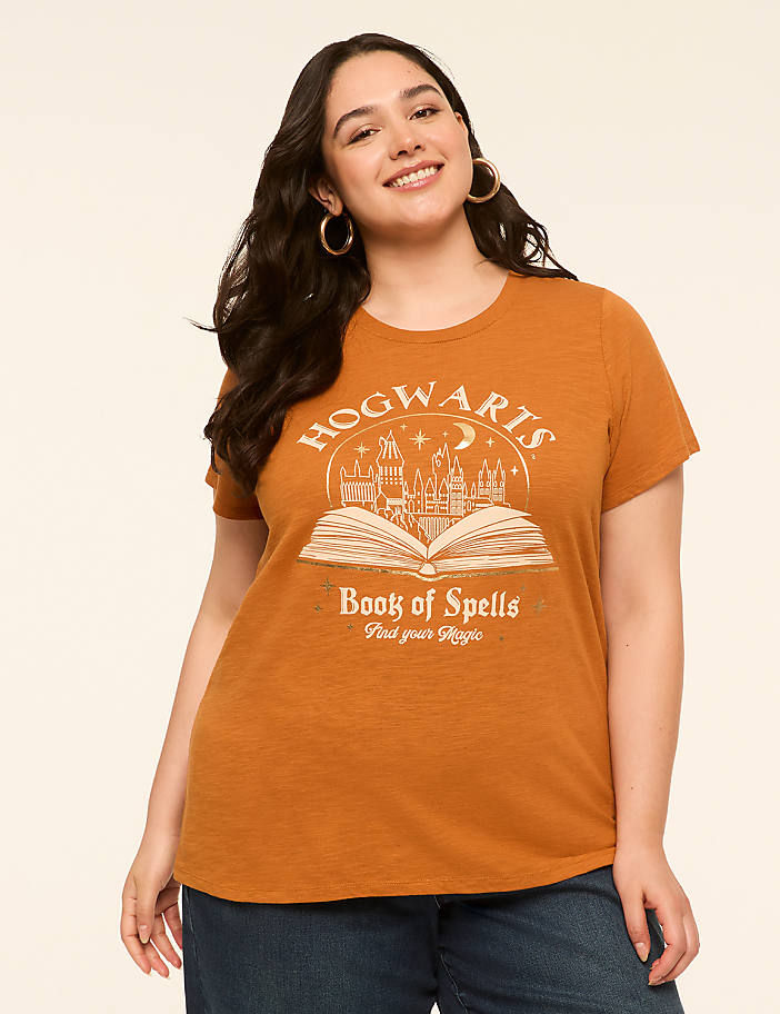 A smiling woman in a Hogwarts t-shirt stands against a plain, light-colored background.