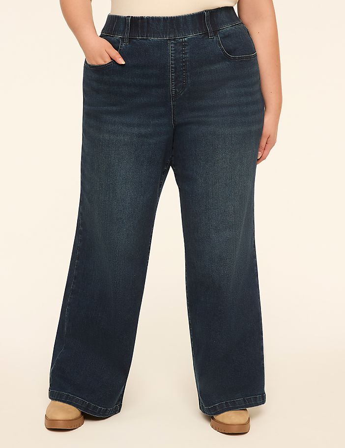 A person wearing dark wash wide-leg jeans stands against a plain, light-colored background.