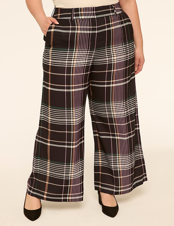 A person stands in wide-leg plaid pants and black heels against a plain, light-colored background.