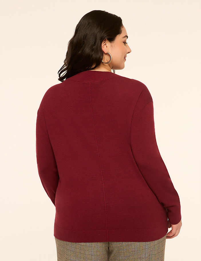 A woman in a maroon cardigan and patterned pants stands against a plain, light-colored background.