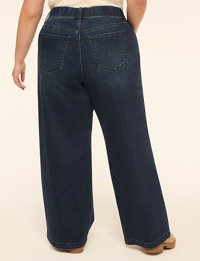 A person wearing dark wash wide-leg jeans stands against a plain, light-colored background.