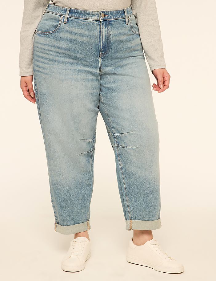 A person in light blue cuffed jeans and white sneakers stands against a plain, light-colored background.