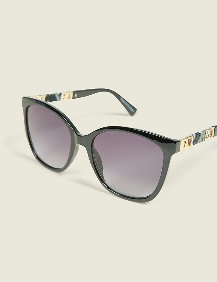 A pair of black, cat-eye sunglasses with marbled temples rests on a plain, light-colored background.