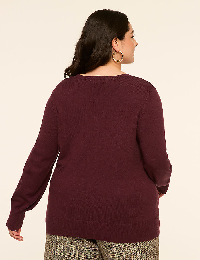 A woman in a maroon sweater and plaid pants stands against a plain, light-colored background.